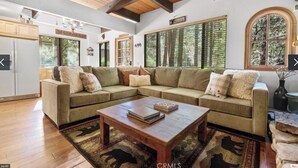 A spacious living room with a sectional sofa, a wooden coffee table, and large windows with blinds.
