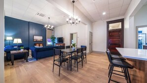 Un salon moderne avec un canapé bleu, un coin repas avec une table et des chaises en bois, et un espace cuisine avec un comptoir en bois et des tabourets de bar.