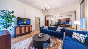 Un salon spacieux doté d’un grand téléviseur à écran plat, d’un canapé bleu, d’un meuble en bois et d’un coin repas à l’arrière-plan.