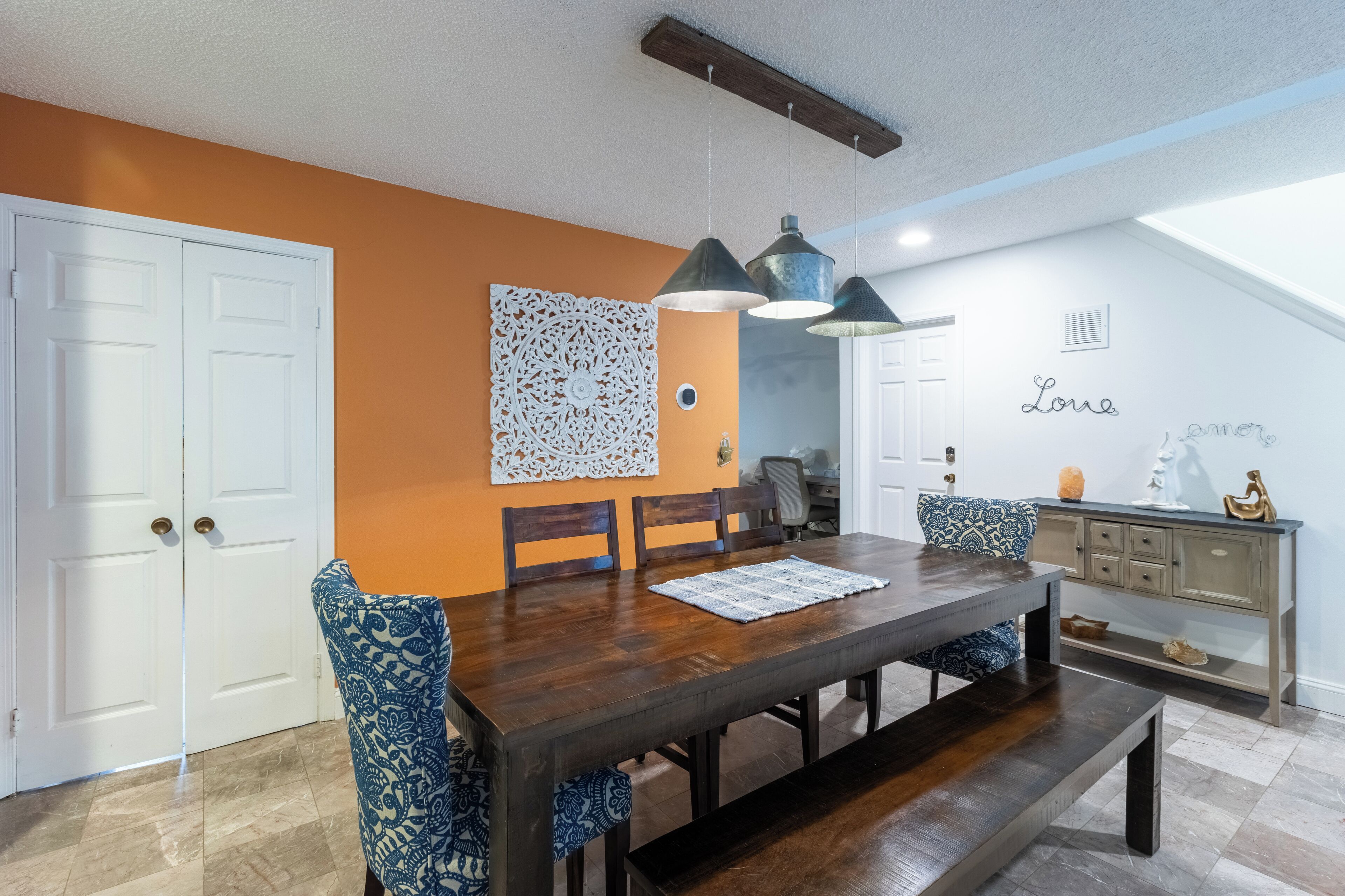 A dining area with a wooden table, blue patterned chairs, pendant lights, and a decorative wall piece.