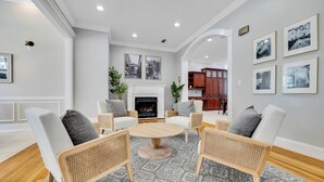 A living room with a round wooden table surrounded by wicker chairs, a fireplace, and framed pictures on the walls. - Conference House Near Emory/CDC w/ Arcade (Atlanta)