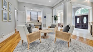 A spacious living room with a large coffee table, comfortable seating, and a view of the exterior through a large window. - Conference House Near Emory/CDC w/ Arcade (Atlanta)