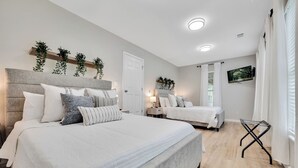 A modern bedroom with two beds, a wooden floor, and a mounted TV. - Conference House Near Emory/CDC w/ Arcade (Atlanta)
