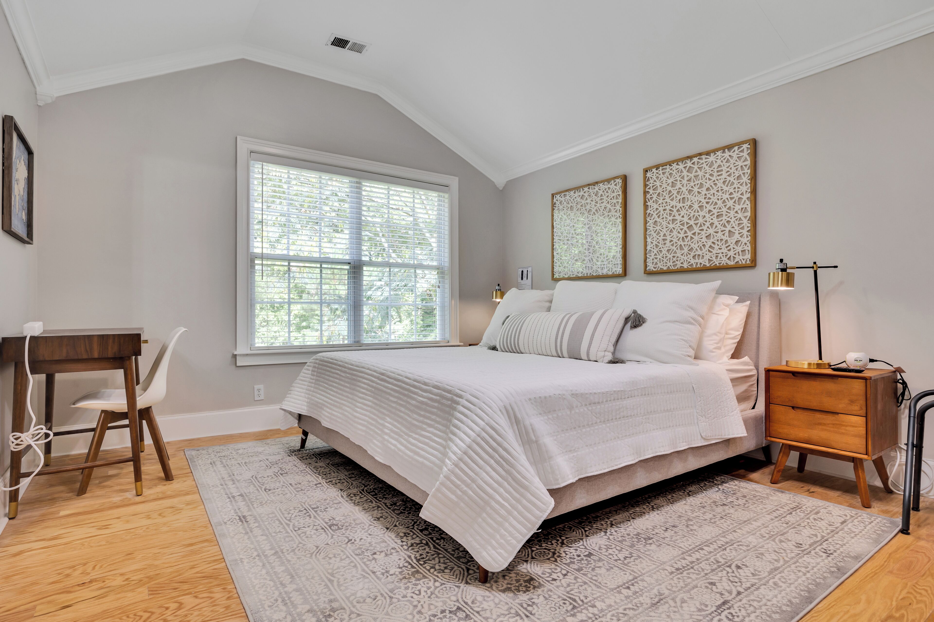 A bedroom with a bed, bedside table, lamp, and a desk with chair.