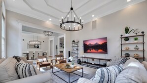 A modern living room with a chandelier, sofas, a coffee table, and a dining area with chairs and a table. - Conference House Near Emory/CDC w/ Arcade (Atlanta)