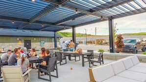 Un patio al aire libre con mesas y sillas, una parrilla y una zona de estar cubierta.