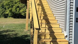Una escalera de madera que sube hacia una casa, con baranda de metal.