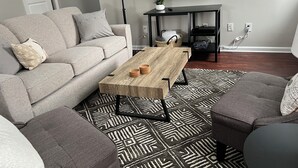 Una sala de estar moderna con un sofá gris, una mesa de centro de madera, una alfombra estampada y un mueble de TV negro.