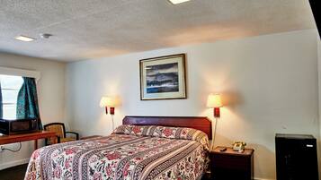 Una habitación de hotel con una cama, lámparas de noche, un escritorio con microondas, un teléfono y un mueble pequeño.