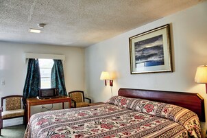 Habitación de hotel con cama, escritorio con microondas, dos sillas, ventana con cortinas e imagen enmarcada en la pared.