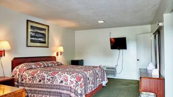 Quarto de hotel com uma cama grande, uma escrivaninha, uma cadeira, uma televisão na parede e um aparelho de ar condicionado.