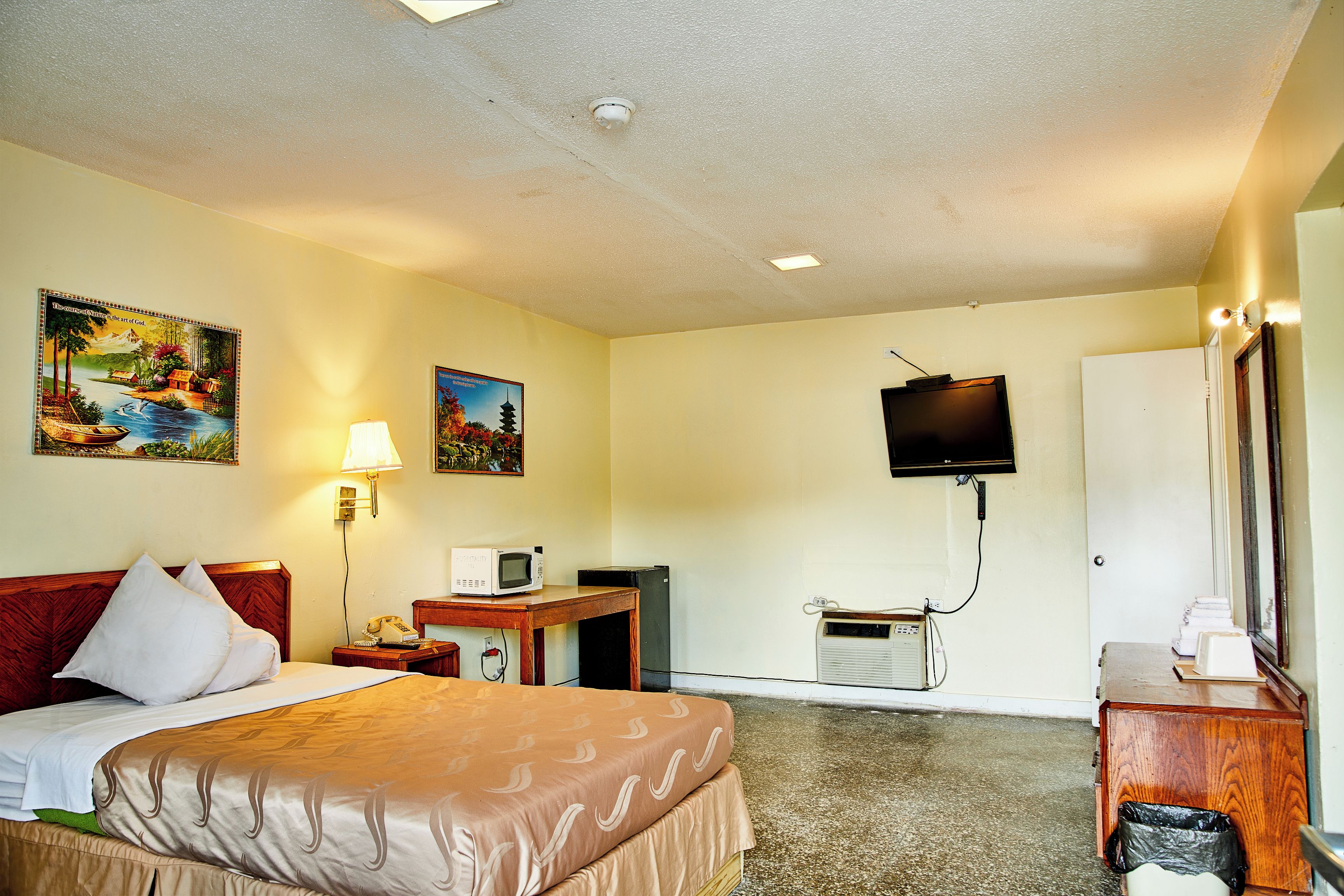 Habitación de hotel con cama, escritorio, televisor y aire acondicionado instalado en la pared.
