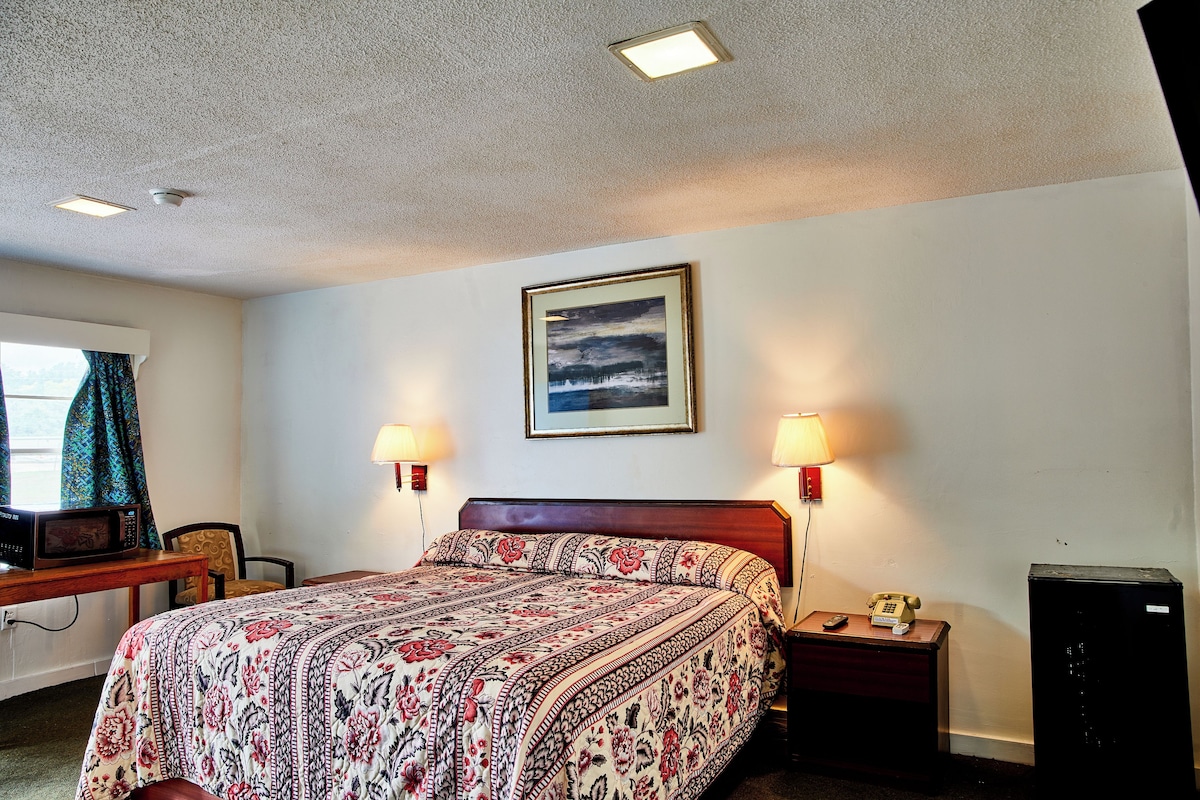 A hotel room with a bed, bedside lamps, a desk with a microwave, a telephone, and a small cabinet.