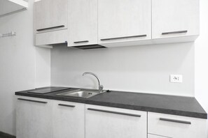 A modern kitchen with white cabinets, a black countertop, and a stainless steel sink.