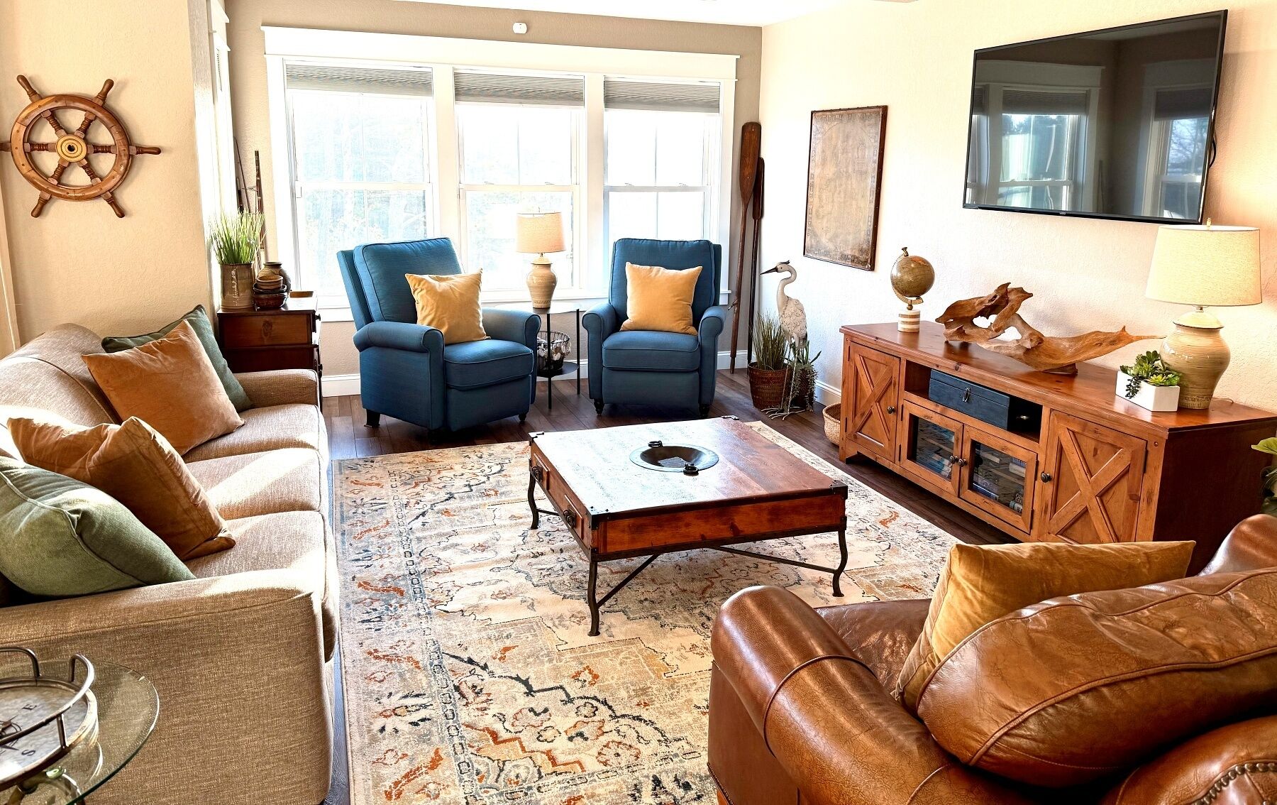 A living room with a sofa, two armchairs, a coffee table, a wooden cabinet, and a TV mounted on the wall.