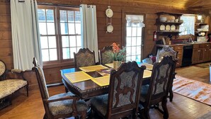 A wooden dining room with a large table and chairs, a kitchen area with wooden cabinets, and a window with curtains. - Rustic but elegant 4-bedroom farmhouse in Canton with WiFi and AC (Canton)