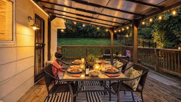 An outdoor patio with a table set for dining, surrounded by chairs, and a wooden deck.