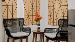 Two wicker chairs with cushions, a small wooden table, and a vase with orange flowers.