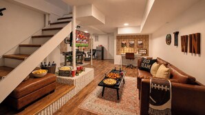 A living room with a brown leather sofa, a coffee table, and a TV. There is a staircase with a wooden handrail and a white wall.