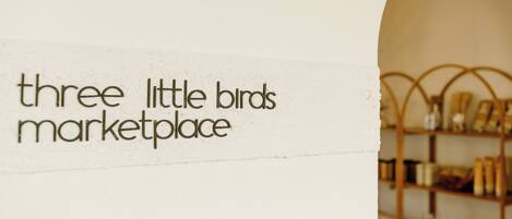 A sign reading "three little birds marketplace" with a wooden shelf in the background.