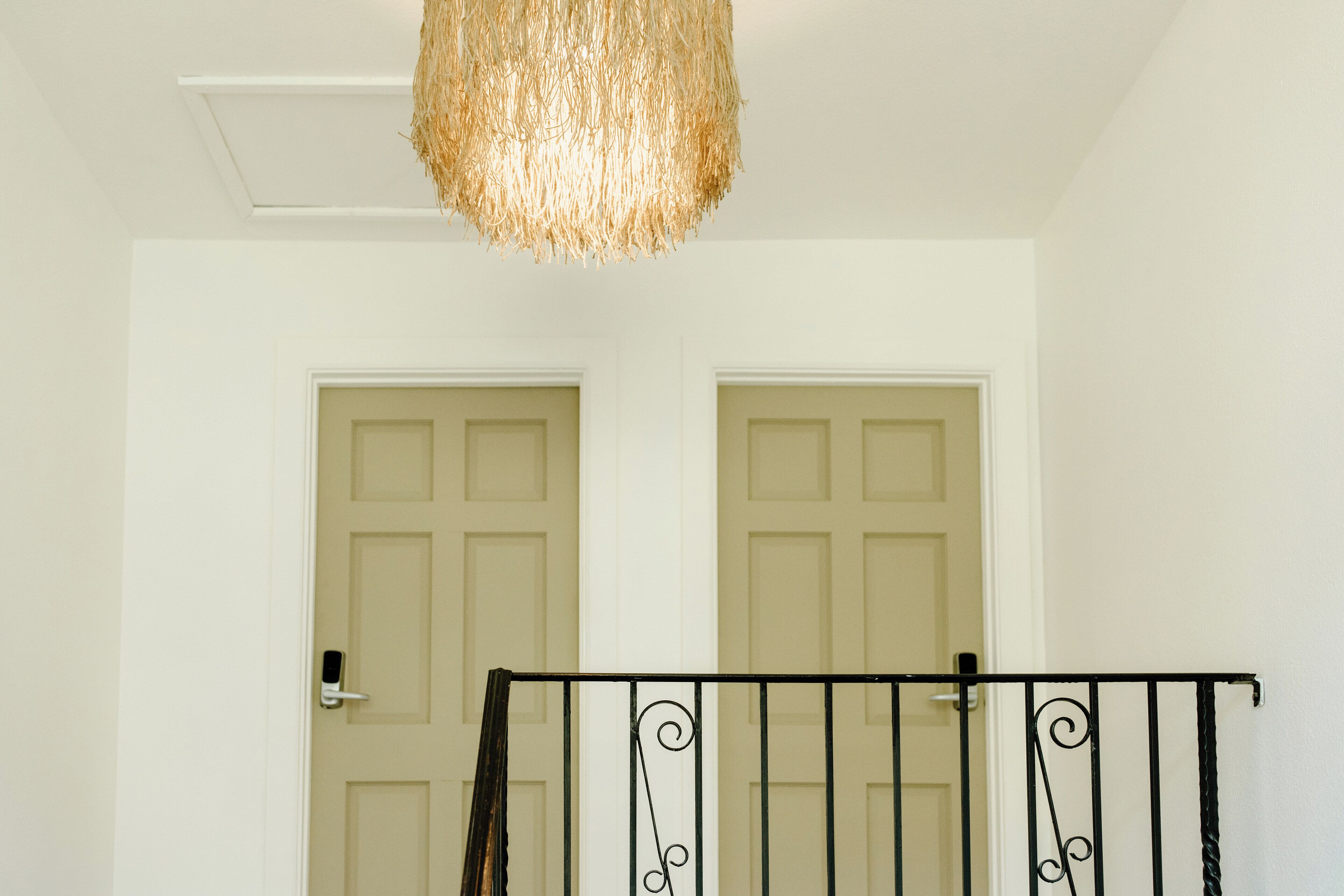 A hallway with two beige doors, a textured ceiling light fixture, and a black metal railing with decorative elements.