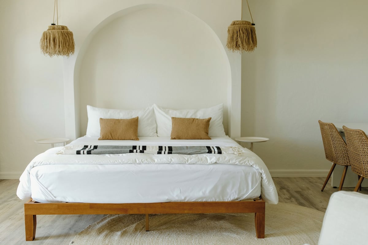 A bedroom with a large bed, two bedside tables, a chair, and a hanging light fixture.