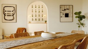 A dining area with a wooden table, wicker chairs, and a white placemat. There are framed artworks on the walls and a plant in the corner. - The Cove Hotel St.Croix  (Christiansted)