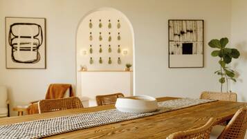 Enjoy meals in this dining area with a wooden table and wicker chairs, surrounded by artwork and a potted plant.