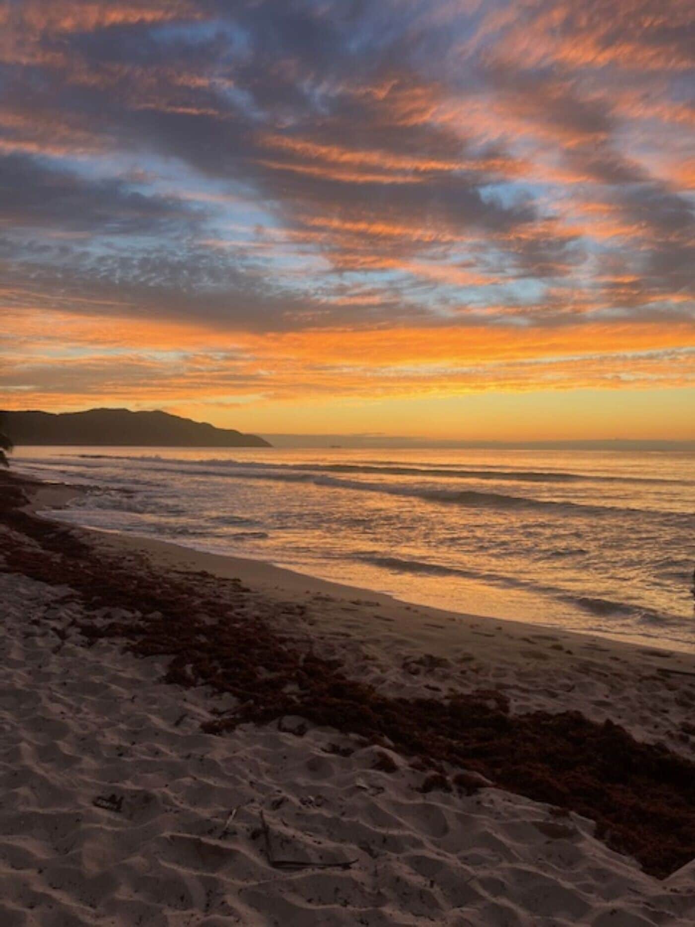 A beach with a sunset, waves, and distant landforms.