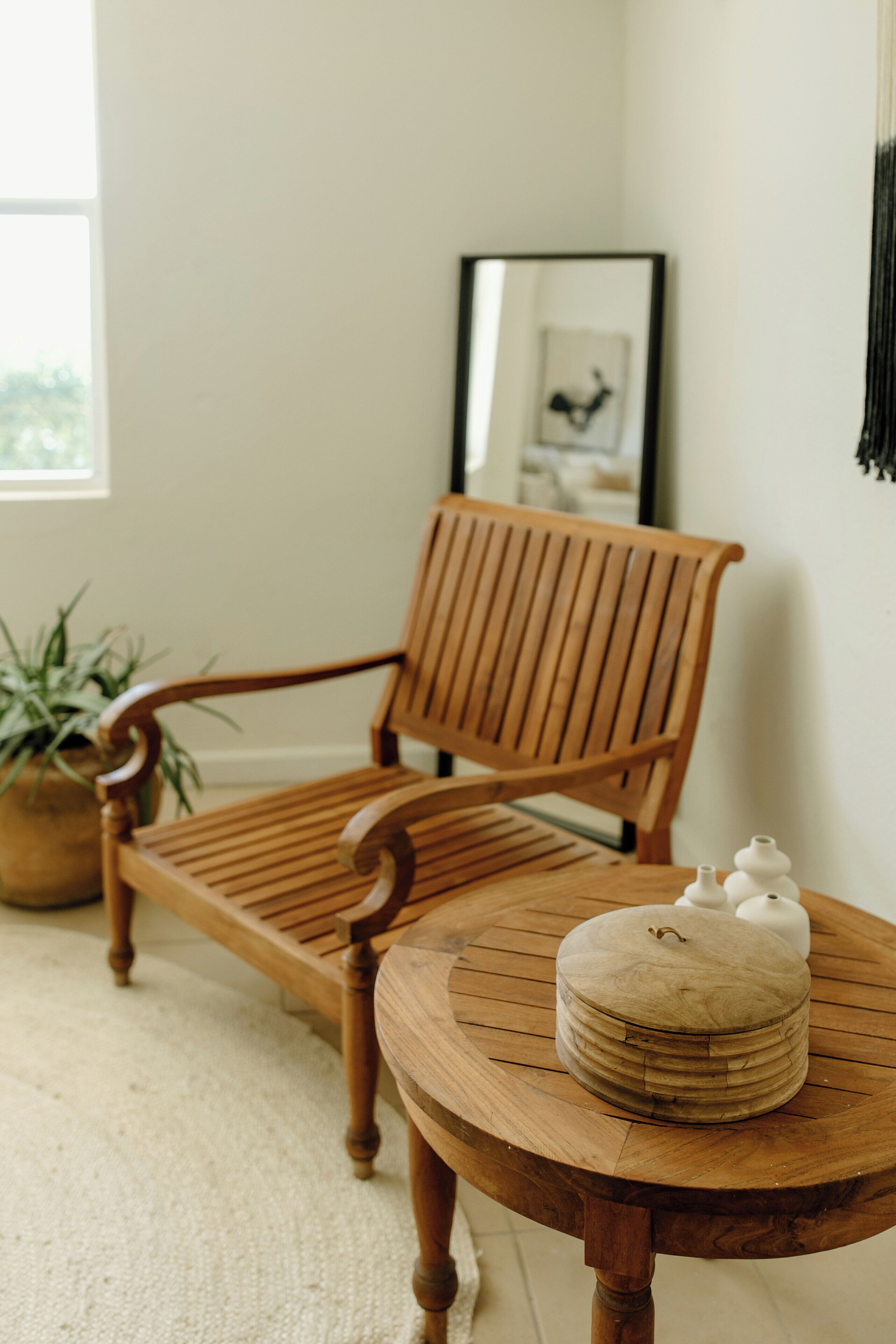 A wooden chair and table in a room with a potted plant and a framed picture on the wall.