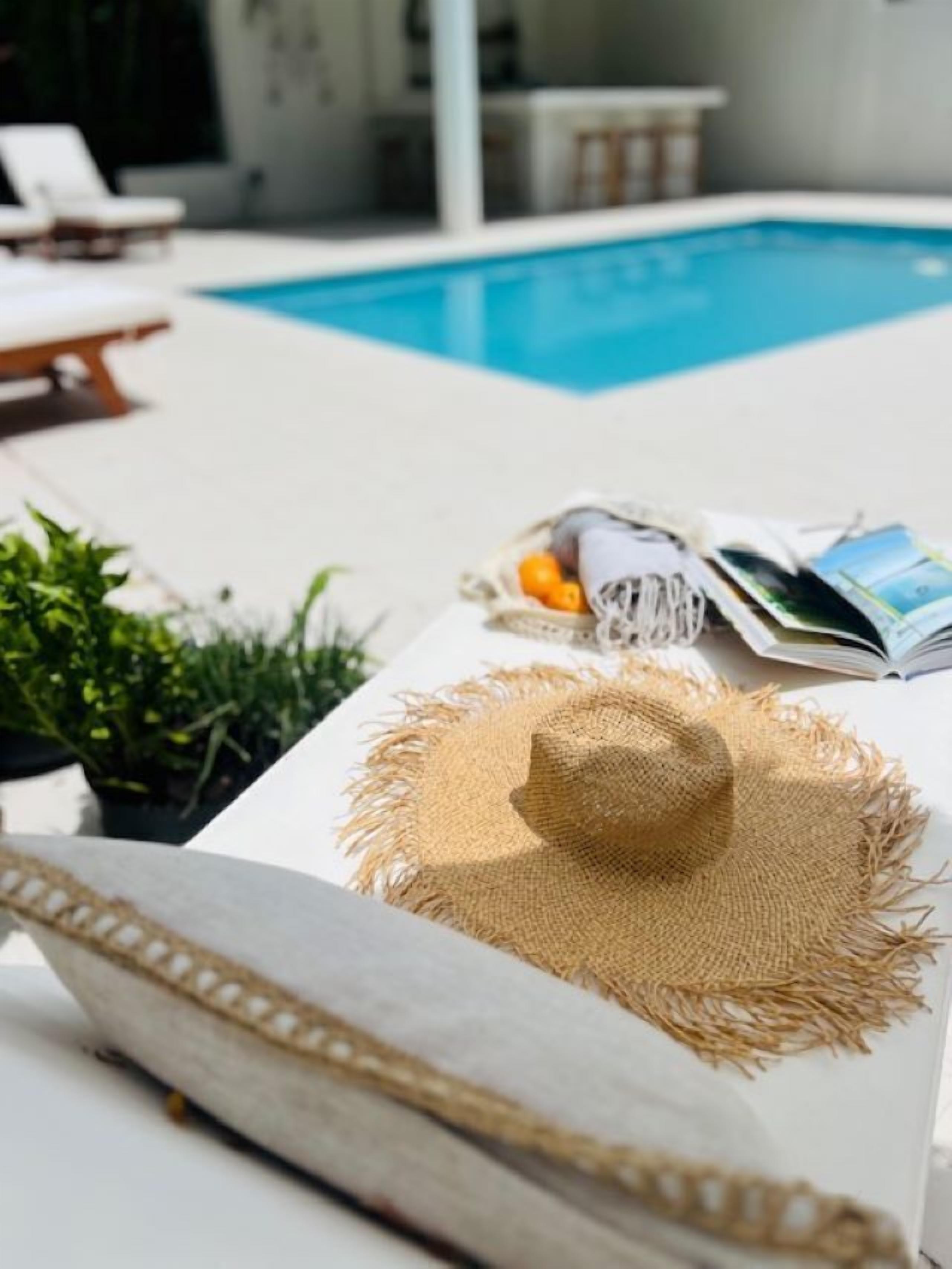 Un espace aménagé au bord de la piscine, avec un fauteuil de relaxation, un chapeau de paille et un petit panier contenant des oranges et des magazines.