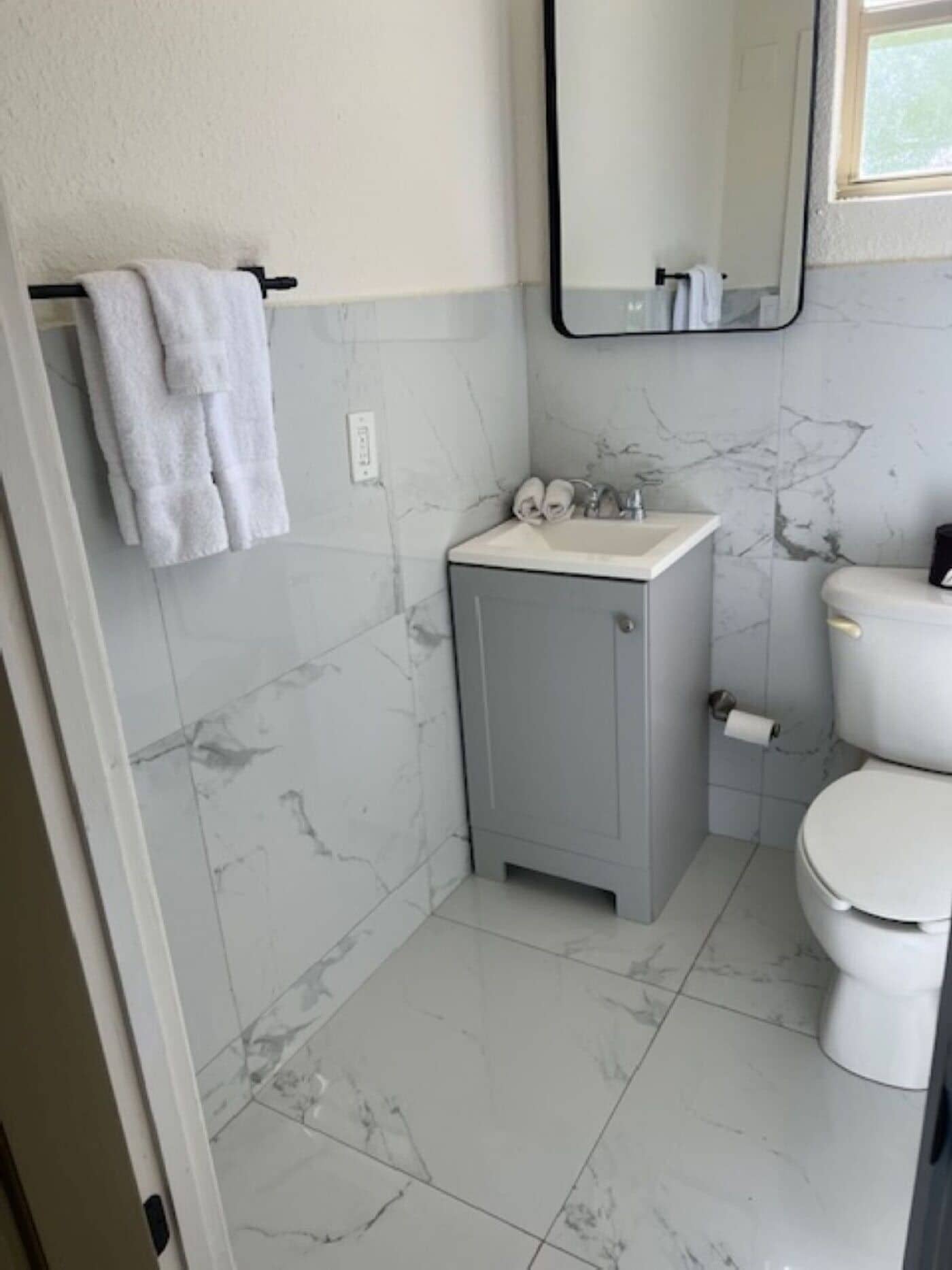A bathroom with a marble floor, a grey cabinet with a sink, a toilet, and a towel rack with towels.