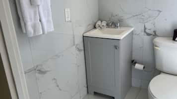A bathroom with a marble floor, a grey cabinet with a sink, a toilet, and a towel rack with towels.