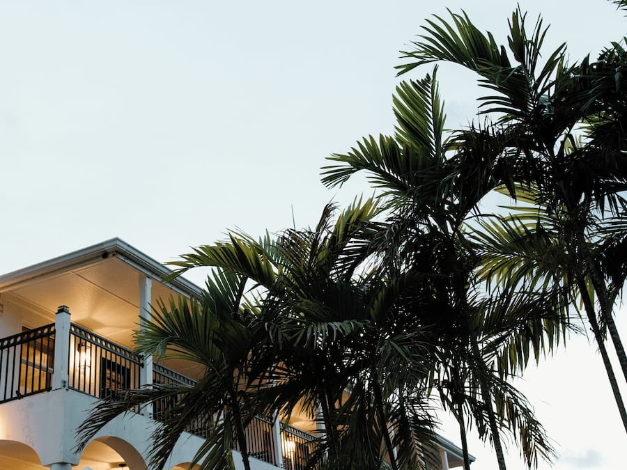 A multi-story building with balconies and arches, surrounded by palm trees.