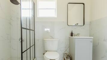 Une salle de bain avec une douche à parois de verre, des toilettes, un lavabo et un miroir.