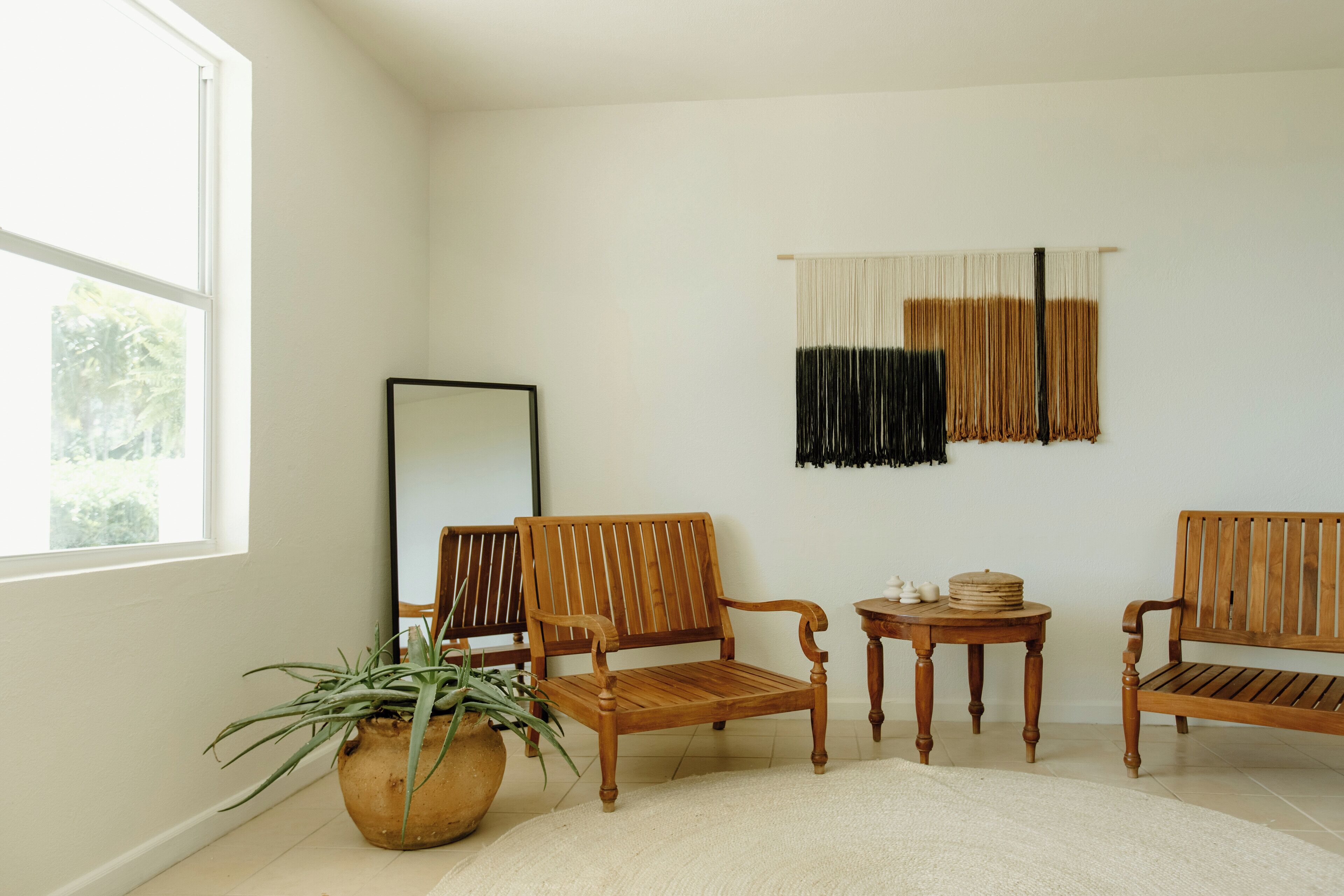 A room with two wooden chairs, a small round table, a potted plant, and a large window.
