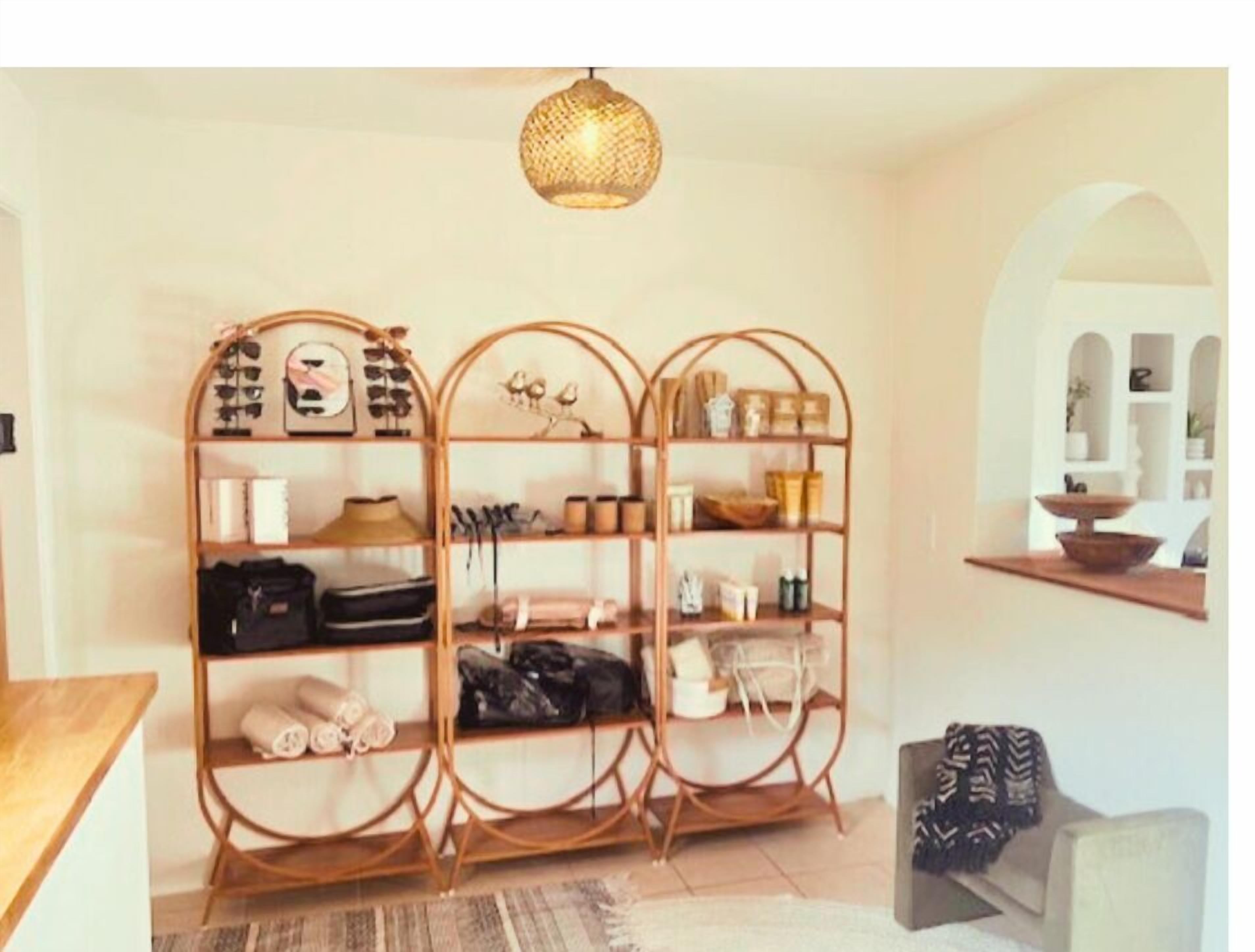A room with a wooden arched shelving unit filled with various items, a hanging woven light fixture, and a view through an arched doorway to another room.