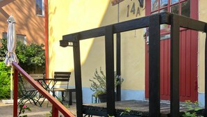 A wooden deck with a bench and a table, a red door, and a yellow wall with the number 14A. - Awesome home in Visby innerstad (Visby innerstad)