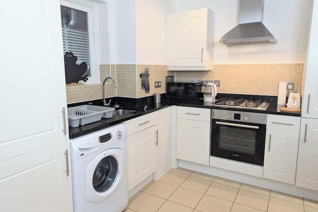 Une cuisine compacte équipée d’un lave-linge, d’un four à micro-ondes, d’une cuisinière et de meubles de rangement blancs.