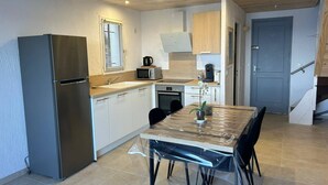 A compact kitchen with a refrigerator, microwave, sink, and stove. There is a dining table with chairs and a vase of flowers. - MINI-VILLA - LEA TARCO - SEA VIEW - AIR CONDITIONING (TARCO CONCA)
