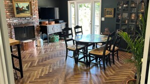 Een eethoek met een visgraat parketvloer, een ronde tafel met stoelen, een open haard van baksteen en een televisie op een meubel.