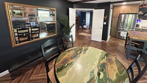 Een eetgedeelte met een ronde tafel en stoelen, een grote spiegel aan de muur, en uitzicht op de keuken.