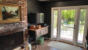 Een kamer met een open haard van baksteen, een televisie en een schuifdeur die leidt naar een terras.