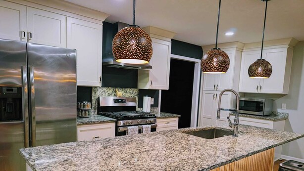 Une cuisine moderne dotée de plans de travail en granit, d’appareils électroménagers en acier inoxydable et de luminaires suspendus.
