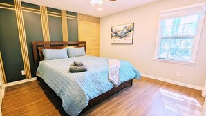 Une chambre à coucher avec un lit, un plancher en bois, un ventilateur de plafond, une fenêtre et des œuvres d’art accrochées au mur.