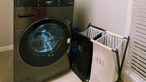 Un lave-linge et un sèche-linge LG à chargement frontal, avec un panier à linge blanc à côté, portant l’inscription « À LUI ».