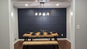 Un coin repas avec un mur lambrissé de couleur bleu foncé, une table en bois surmontée de bols noirs et un luminaire suspendu.