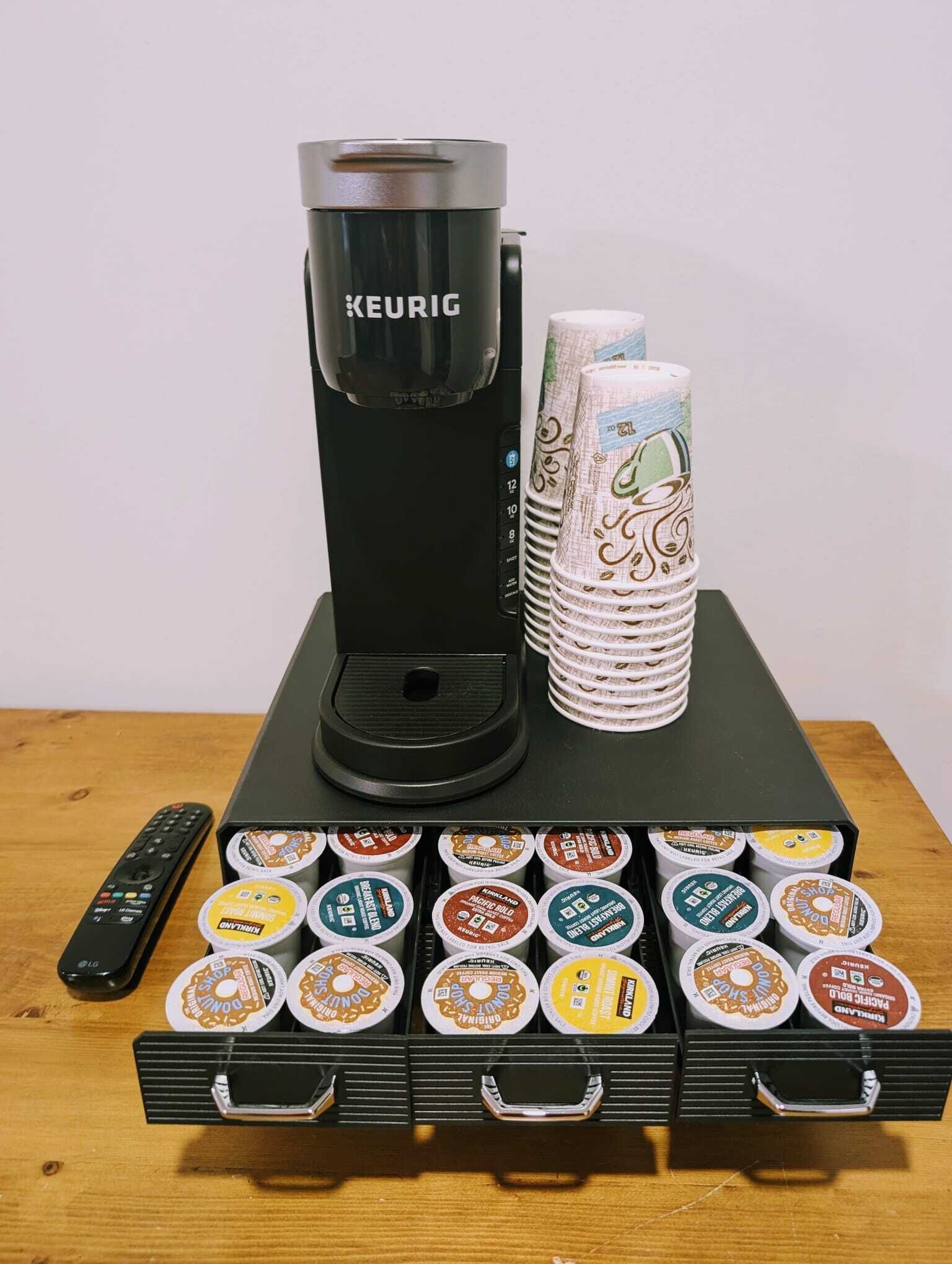Een Keurig koffiezetapparaat, koffiefilters en een afstandsbediening op een houten tafel.