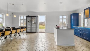 Une cuisine spacieuse dotée d’un grand îlot central, d’un coin repas avec des chaises et d’une vue sur l’extérieur grâce à une porte.