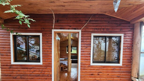 Une cabane en rondins avec une façade en bois, une porte d’entrée centrale et deux fenêtres à cadres blancs.